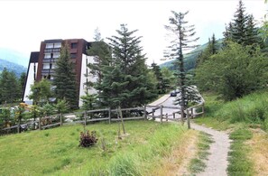 Ein Gebäude im modernen Stil, umgeben von bewaldeter Landschaft mit einem Feldweg, der zur Straße führt.