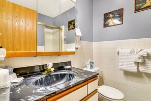 Un baño con tocador de madera, un lavamanos con dispensador de jabón, un inodoro y un perchero para toallas.