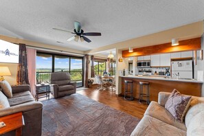 A spacious living room with a large window, a ceiling fan, and a kitchen area with modern appliances. - Lake View Retreat with Boat Slip Included & Free Silver Dollar City Tickets (Branson)