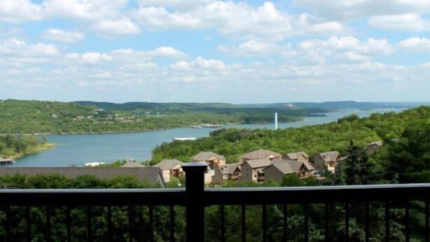 A view of a lake with surrounding greenery and a few buildings.