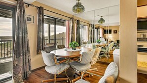 A spacious conference room with a round table, grey upholstered chairs, and large windows offering a view of the outdoors.