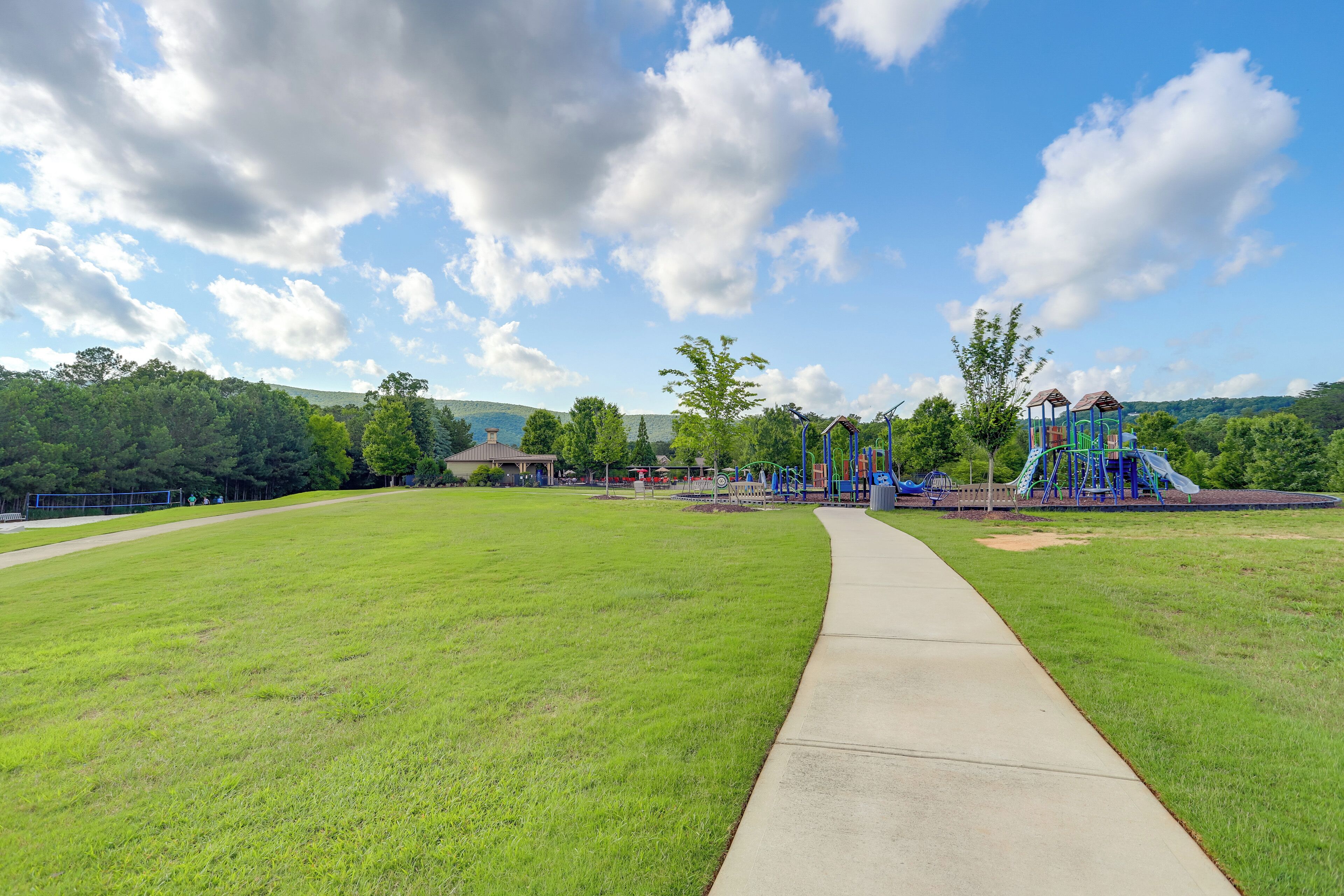 A park with a concrete path, playground equipment, and trees.