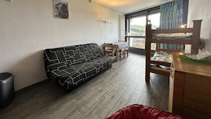 Una habitació amb un sofà, una taula de dinar amb cadires, un armari de fusta i una finestra amb vistes.