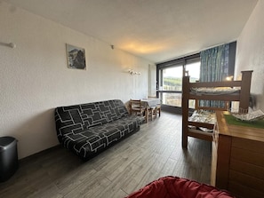 A room with a sofa, a dining table with chairs, a wooden cabinet, and a window with a view. - 7th floor, balcony, parking, tv, 24m², Villard de Lans (Villard-de-Lans)