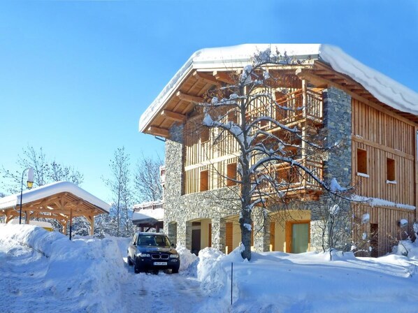 Un immeuble à plusieurs étages, doté d’une façade en pierre et de balcons en bois, entouré de neige.