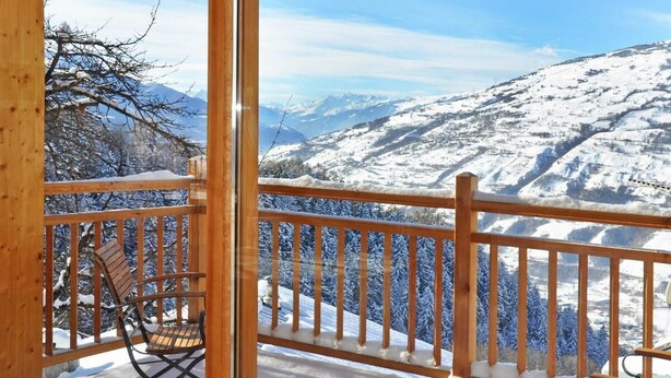 A wooden deck with a railing, two wooden chairs, and a view of snow-covered mountains. - Chalet, wifi, sauna, terrace, balcony, fireplace or stove, parking, tv, 250m², Les Arcs (Bourg-Saint-Maurice)