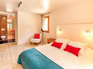 Une chambre d’hôtel avec un grand lit, une chaise, une table de chevet et une salle de bain visible à travers une porte ouverte.