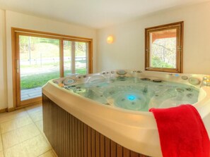 Un bain à remous dans une pièce dotée de grandes fenêtres donnant sur un paysage verdoyant.