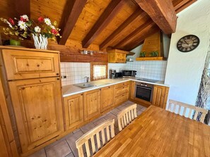 Uma cozinha rústica com painel de azulejos, armários de madeira, mesa de jantar de madeira e um relógio na parede.