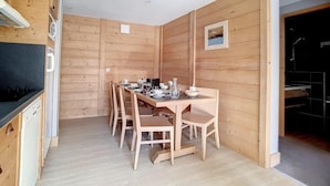 A wooden-paneled room with a dining table set for four, a kitchen area with a dishwasher, and a framed picture on the wall.