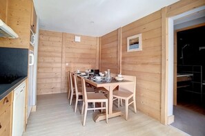 A wooden-paneled room with a dining table set for four, a kitchen area with a dishwasher, and a framed picture on the wall.