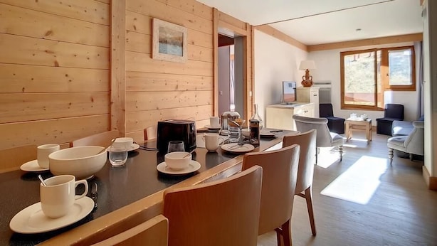 A wooden-paneled room with a dining table set for four, a kitchen area with a stove and cabinets, and a seating area with chairs and a sofa.