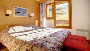 A bedroom with a large bed, a window with a view of a landscape, and a framed picture on the wall.