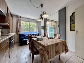A dining area with a table set for four, a kitchen with cabinets and appliances, and a blue sofa in the background.