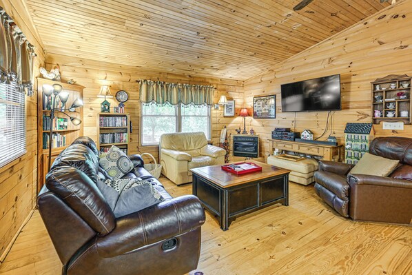Ein gemütliches Holzblockhaus-Interieur mit Ledersofas, einem Fernseher, Bücherregalen und einem Kamin.