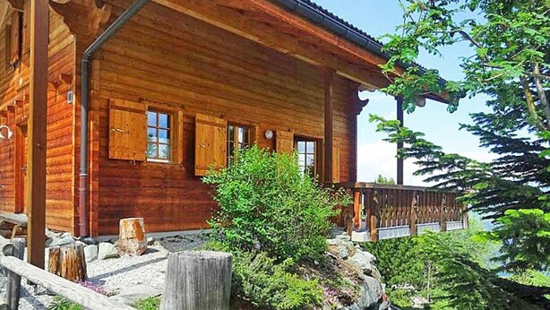 Una cabaña de madera con porche, rodeada de vegetación y un sendero de piedra.