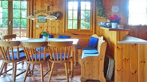 Interior de una cabaña de madera con comedor, mostrador de cocina y ventana con vistas a la vegetación.