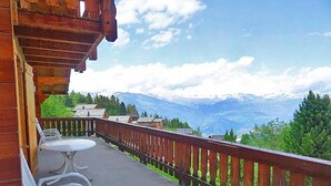 Terraza de madera con mesa y sillas, con vistas a un paisaje montañoso.