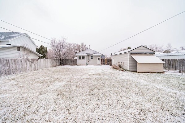 A residential backyard with a house, a detached garage, and a wooden fence.