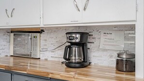 Een keuken met witte kastjes, een koffiezetapparaat en een bord met informatie over koffie benodigdheden.