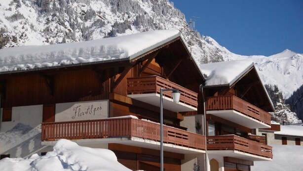 Un chalet en bois doté de nombreux balcons, entouré de montagnes enneigées.