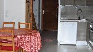 Une cuisine chaleureuse avec un évier et une cuisinière modernes, un coin repas avec une nappe à carreaux et un escalier en bois menant à l’étage supérieur.