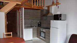 Une cuisine compacte équipée d’un lave-vaisselle, d’un four et d’un four à micro-ondes. On y trouve une chaise en bois et une table recouverte d’une nappe à carreaux.