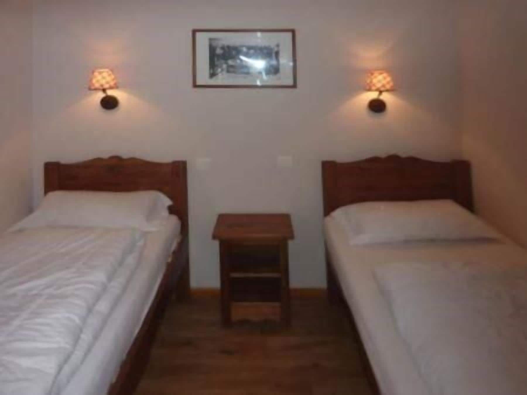 Una habitación con dos camas individuales, una mesita de noche de madera y dos lámparas de pared.