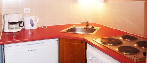 A compact kitchen with wooden cabinets, a red countertop, a built-in microwave, a coffee maker, a sink, and a dishwasher.