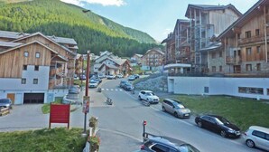 Ein Bergdorf mit Holzbauten, einer Hauptstraße und Blick auf grüne Hügel.