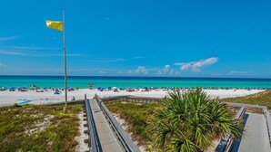 A beach with a wooden boardwalk, a flag, and a palm tree. - 2 min to the beach with 30A's largest pool, plus stunning decks, and 4 bikes (Santa Rosa Beach)