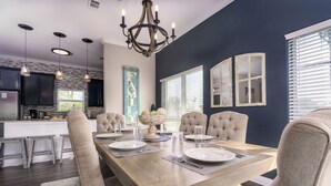 A dining area with a wooden table, beige upholstered chairs, and a chandelier. - 2 min to the beach with 30A's largest pool, plus stunning decks, and 4 bikes (Santa Rosa Beach)