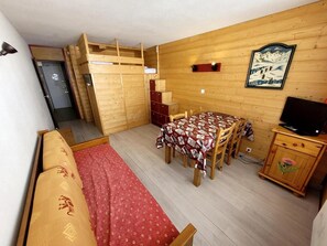 A compact room with a bunk bed, a dining table with chairs, a television, and a wooden cabinet. - 10m from ski slopes, view ski slopes, balcony, tv, 25m², La Plagne (La Plagne)