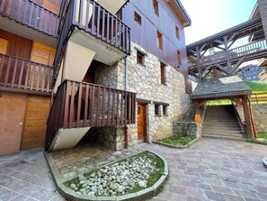 Un edificio de varios pisos con fachada de piedra, balcones de madera y una escalera de piedra que conduce a un nivel superior.