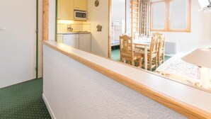 Une pièce avec un plafond en bois, une table à manger avec des chaises, un coin cuisine avec des placards et un four à micro-ondes, et une fenêtre avec des rideaux.