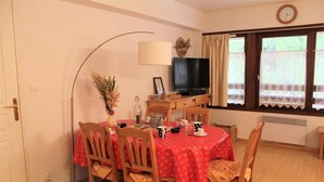 A dining area with a round table covered by a red tablecloth, surrounded by wooden chairs. A television is mounted on the wall above the table. - 250m from ski slopes, 6th floor, parking, tv, ski locker, 50m², Vars (Vars)