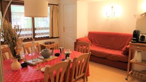 A cozy living room with a red sofa, a dining table with chairs, and a coffee machine on a side table. - 250m from ski slopes, 6th floor, parking, tv, ski locker, 50m², Vars (Vars)