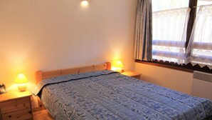 A bedroom with a bed, two bedside lamps, a wooden nightstand, and a window with curtains. - 250m from ski slopes, 6th floor, parking, tv, ski locker, 50m², Vars (Vars)