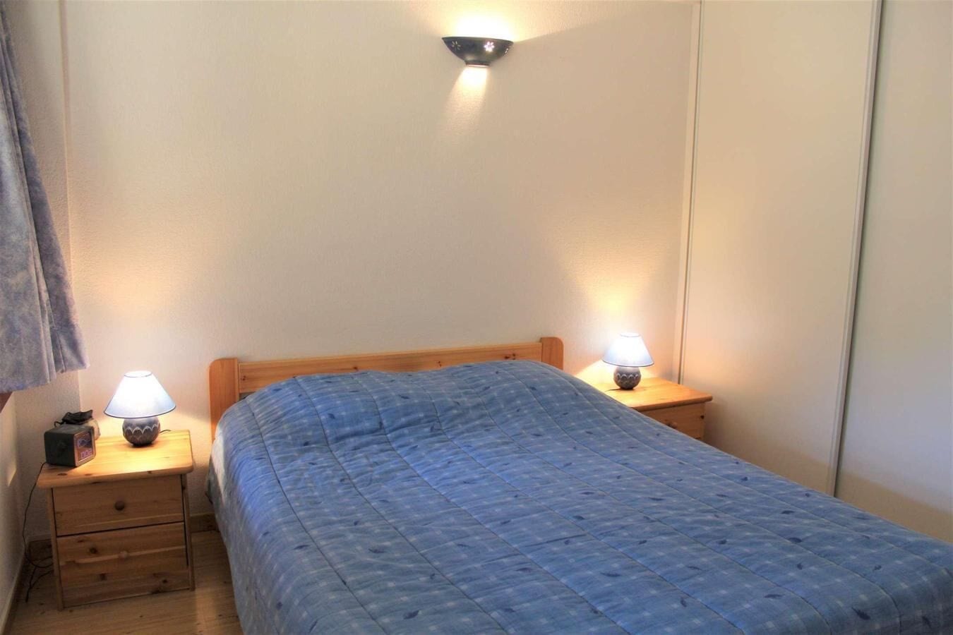 Une petite chambre à coucher simple, avec un lit simple, deux tables de chevet avec des lampes et un luminaire fixé au mur.