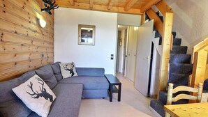 A cozy living room with a grey sectional sofa, a small table, and a wooden staircase. - 10m from ski slopes, 3rd floor, balcony, ski locker, 41m², Méribel-Mottaret (Méribel - Les Allues)