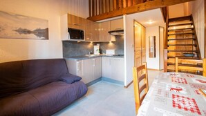 A compact living space with a kitchenette, a sofa, a dining table, and a staircase.
