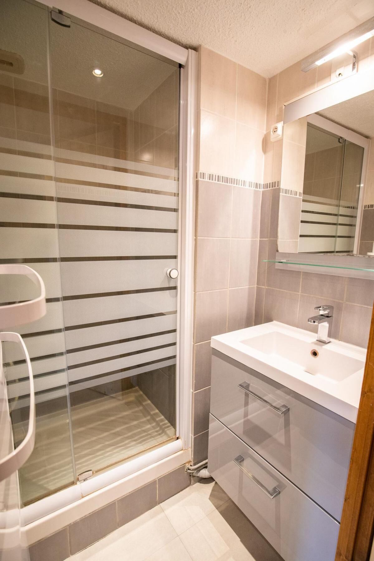 A bathroom with a glass shower enclosure, a white sink, and a mirror above the sink.