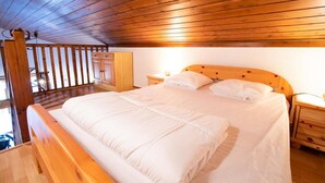 A bedroom with a wooden ceiling, a bed with white bedding, wooden nightstands, and a wooden wardrobe.