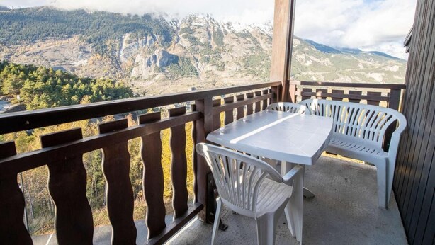 A balcony with a table and two chairs, overlooking a mountainous landscape.