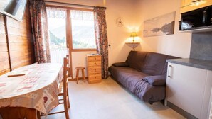 A cozy room with a dining table, a sofa, a small stool, a wooden dresser, and a kitchen area with a microwave.