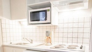 Et kompakt køkken med hvide skabe, en mikrobølgeovn, kaffemaskine og opvaskemaskine.