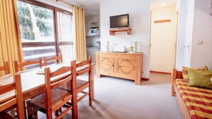 A room with a wooden dining table and chairs, a wooden cabinet with a television above it, a microwave, and a sofa with a plaid blanket. - 130m from ski slopes, 4th floor, balcony, parking, tv, ski locker, 35m², La Norma (La Norma)