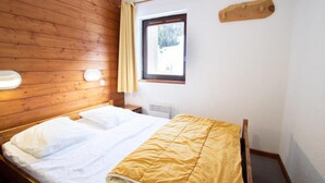 Une pièce avec un mur en bois, un lit avec une literie blanche et jaune, une fenêtre donnant sur des arbres et un luminaire fixé au mur.