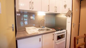 Una kitchenette compacta con gabinetes blancos, un lavamanos de acero inoxidable y un horno empotrado.