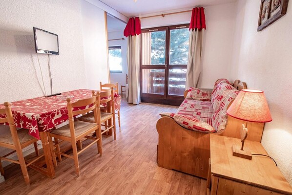 Un salon chaleureux avec un canapé en bois, une table à manger avec des chaises et un téléviseur fixé au mur.
